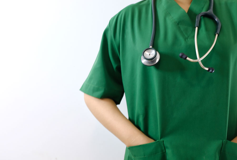 Człowiek w fartuchu lekarskim w kolorze zielonym, na szyi ma zawieszony stetoskop.